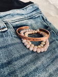 Don’t be a jerk copper bracelet displayed with beaded bracelets on top of jeans